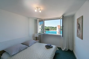 A bedroom with a bed, a window with curtains, a bedside lamp, and a painting on the wall. - Apartments Lapa (Tisno)