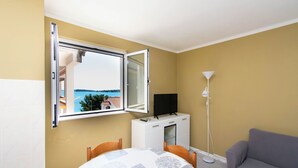 A room with a dining table, chairs, a sofa, a TV on a cabinet, a standing lamp, and a window with an open view. - Apartments Lapa (Tisno)