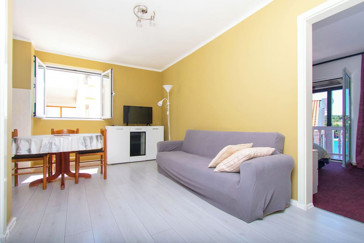 A living room with a sofa, a dining table with chairs, a TV, and a lamp.