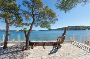 A bench overlooking a body of water with a stone-paved area and a white railing. - Apartments Lapa (Tisno)