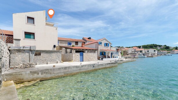 Un pueblo costero con edificios de piedra, agua cristalina y mar en calma.