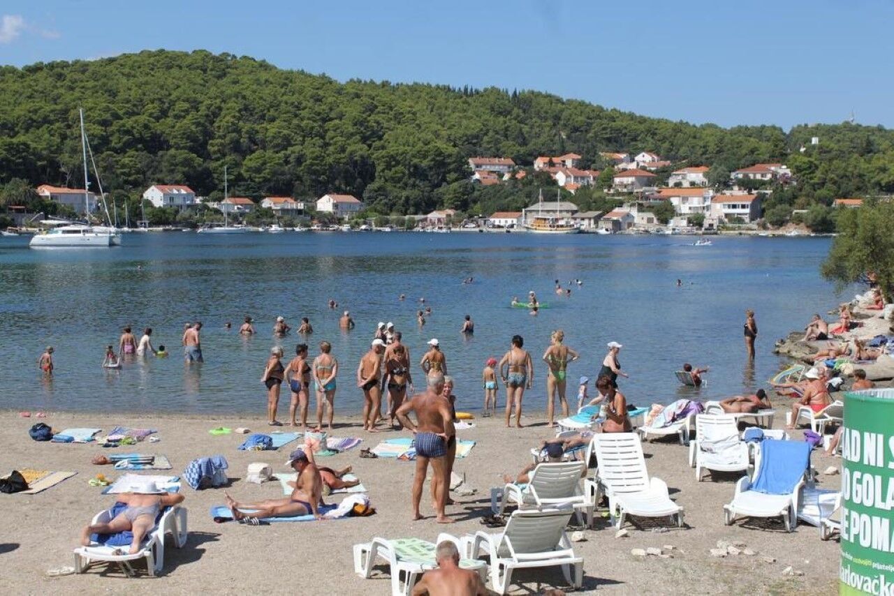 A beach with people swimming and sunbathing, surrounded by houses and a hill in the background.
