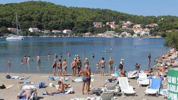 A beach with people swimming and sunbathing, surrounded by houses and a hill in the background.