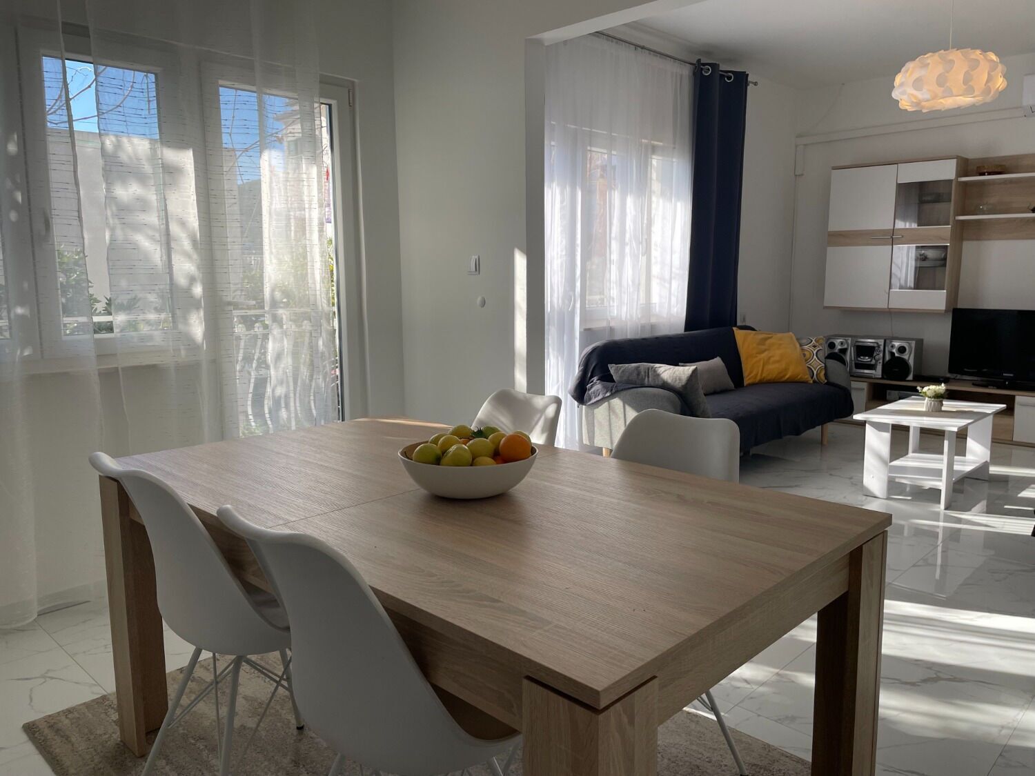 Een moderne woonkamer met een eethoek, met een houten tafel, witte stoelen, een bank en een televisie.