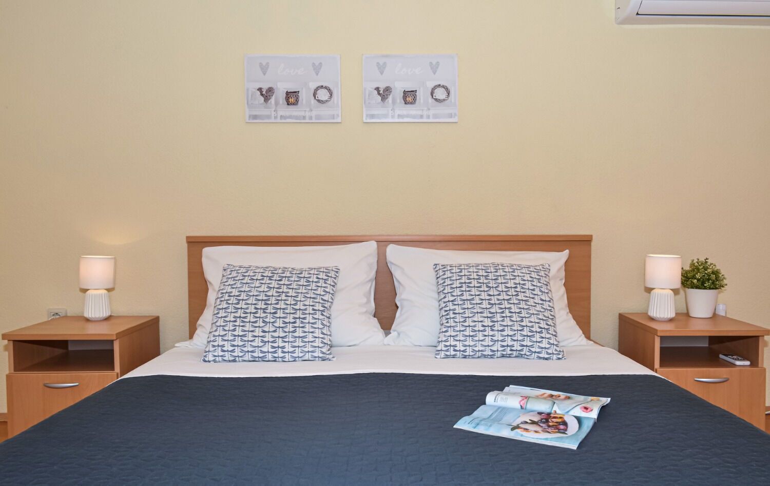 A neatly made bed with patterned pillows, a magazine on the bed, and two wall decorations with the word "love".