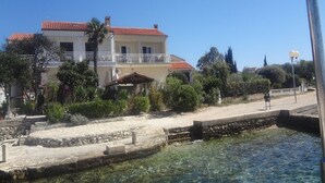 A two-story building with a red-tiled roof, a balcony, and a stone pathway leading to a body of water. - Apartment Andri (Zadar)