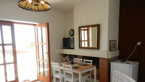 A dining area with a wooden table and white chairs, a television above the fireplace, and a clock on the wall. - Apartment Andri (Zadar)