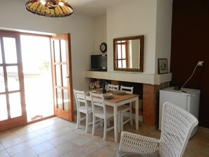 A dining area with a wooden table and white chairs, a television above the fireplace, and a clock on the wall. - Apartment Andri (Zadar)