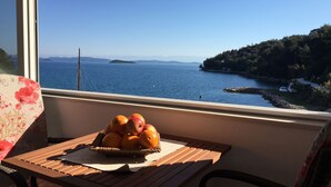 A balcony with a table holding a basket of fruit, overlooking a coastal view with a clear sky and distant islands. - Apartments Durda (Sali)