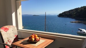 A balcony with a table holding a fruit basket, overlooking a calm sea with a boat and a distant island. - Apartments Durda (Sali)