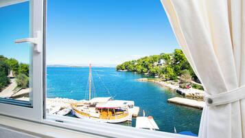 Vista costeira através de uma janela com cortina, mostrando uma marina com barcos e um céu azul límpido.