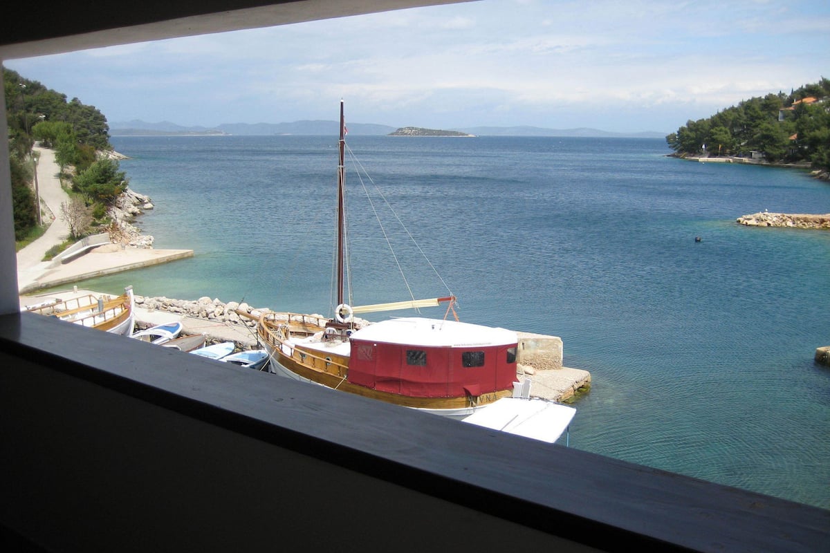 Vista costera con un muelle, barcos y un pequeño edificio.