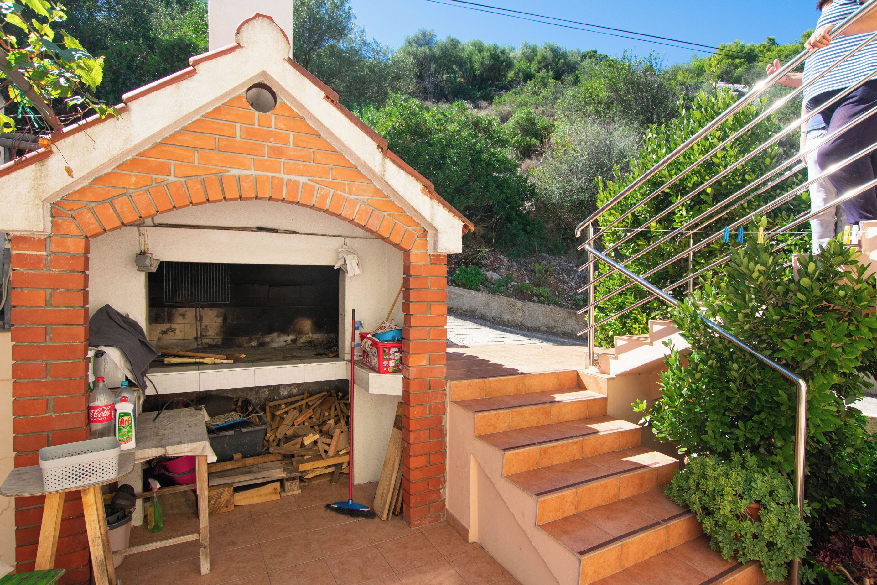 Una cocina exterior de ladrillo con chimenea, una mesa con productos de limpieza y una escalera que conduce a un nivel superior.