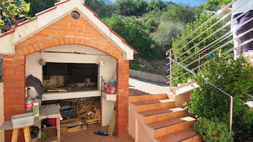 Una cocina exterior de ladrillo con chimenea, una mesa con productos de limpieza y una escalera que conduce a un nivel superior.