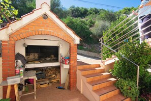 A brick-built outdoor kitchen with a chimney, a table with cleaning supplies, and a staircase leading to a higher level. - Apartments Durda (Sali)