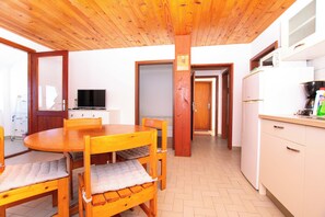 A wooden dining table with chairs, a television, and a kitchen area with cabinets and appliances. - Apartments Durda (Sali)