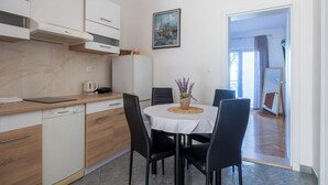 A modern kitchen with a dishwasher, a coffee maker, and a dining area with a table and chairs. - Apartments Josip (Baska Voda)