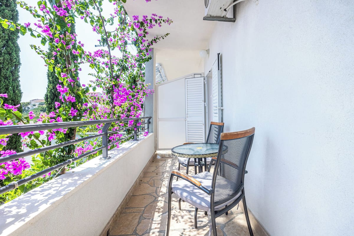 A balcony with a table and chairs, surrounded by purple flowers and a metal railing.
