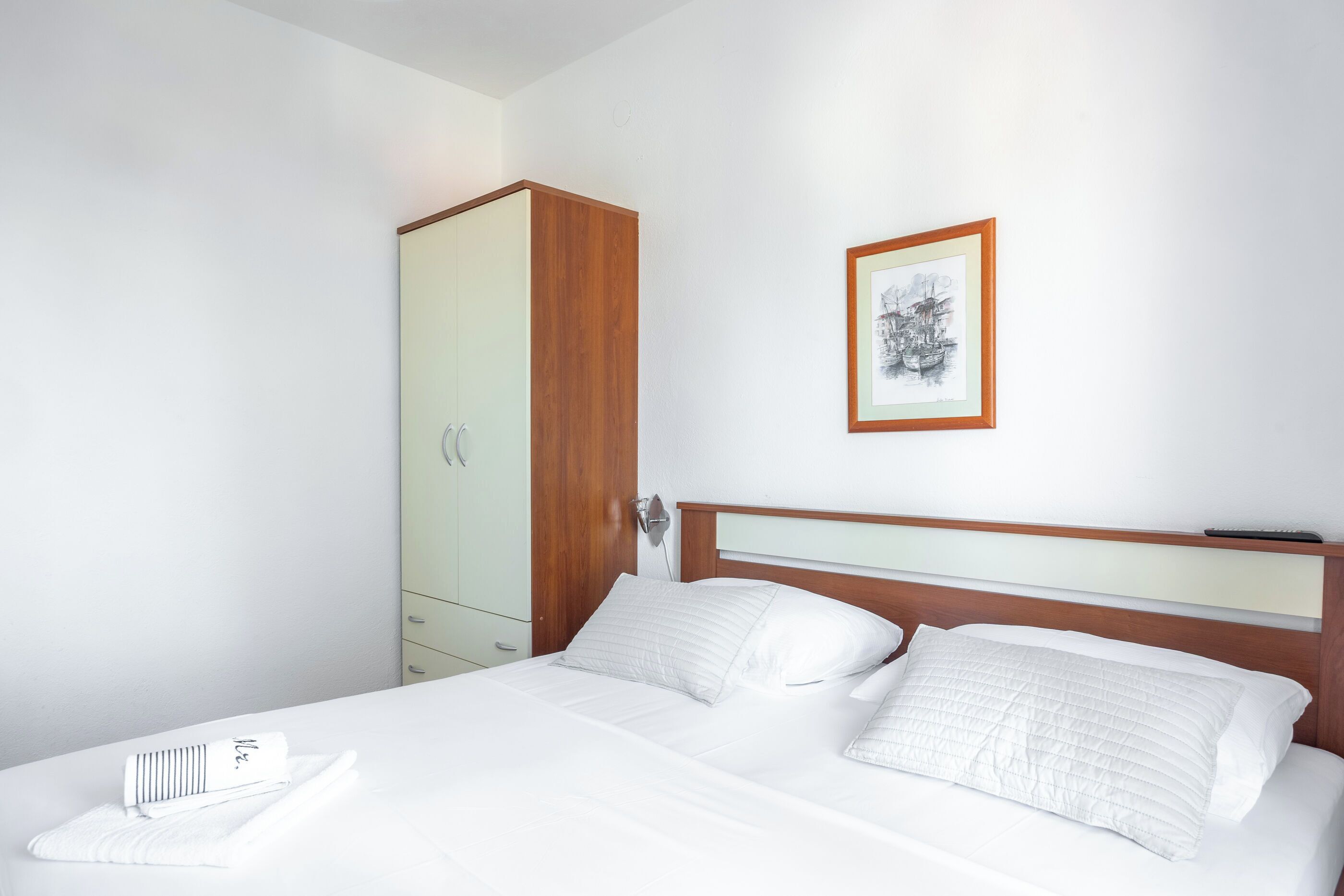 A neatly made bed with white linens, a wooden headboard, and a framed picture on the wall.