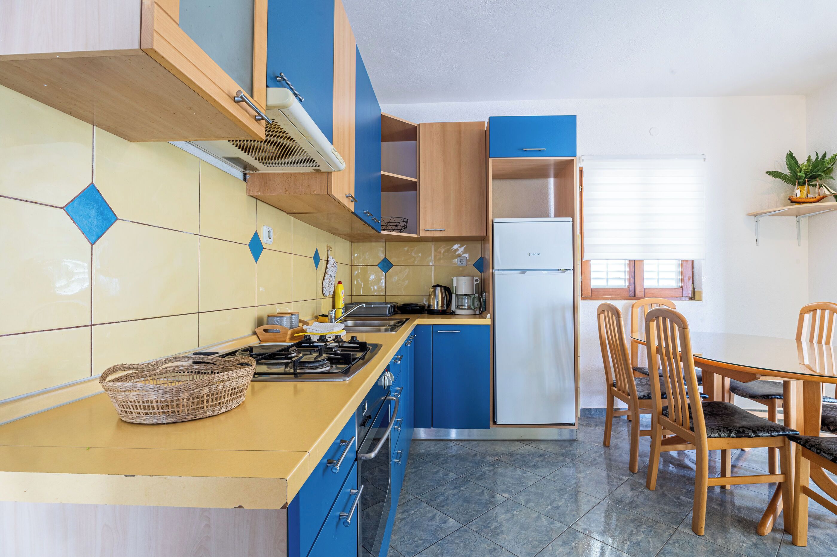 A kitchen with blue cabinets, a stove, a sink, and a dining area with wooden chairs.