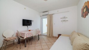 Une chambre d’hôtel comprenant un lit, un téléviseur fixé au mur, une table à manger avec des chaises et une fenêtre avec des rideaux.