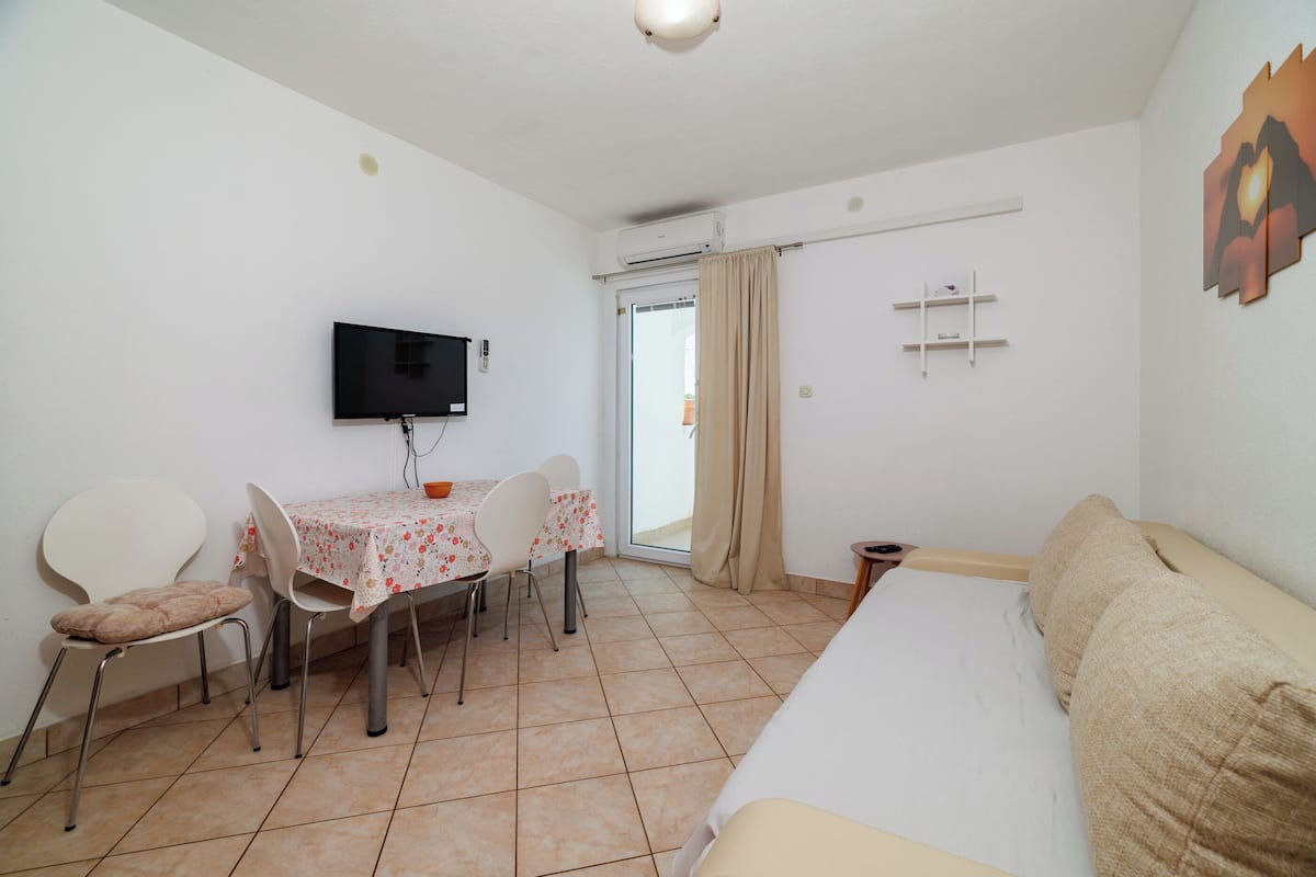 Habitación de hotel con cama, televisión montada en la pared, mesa de comedor con sillas y ventana con cortinas.