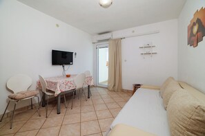 Ein Hotelzimmer mit Bett, Wandfernseher, Esstisch mit Stühlen und einem Fenster mit Vorhängen.
