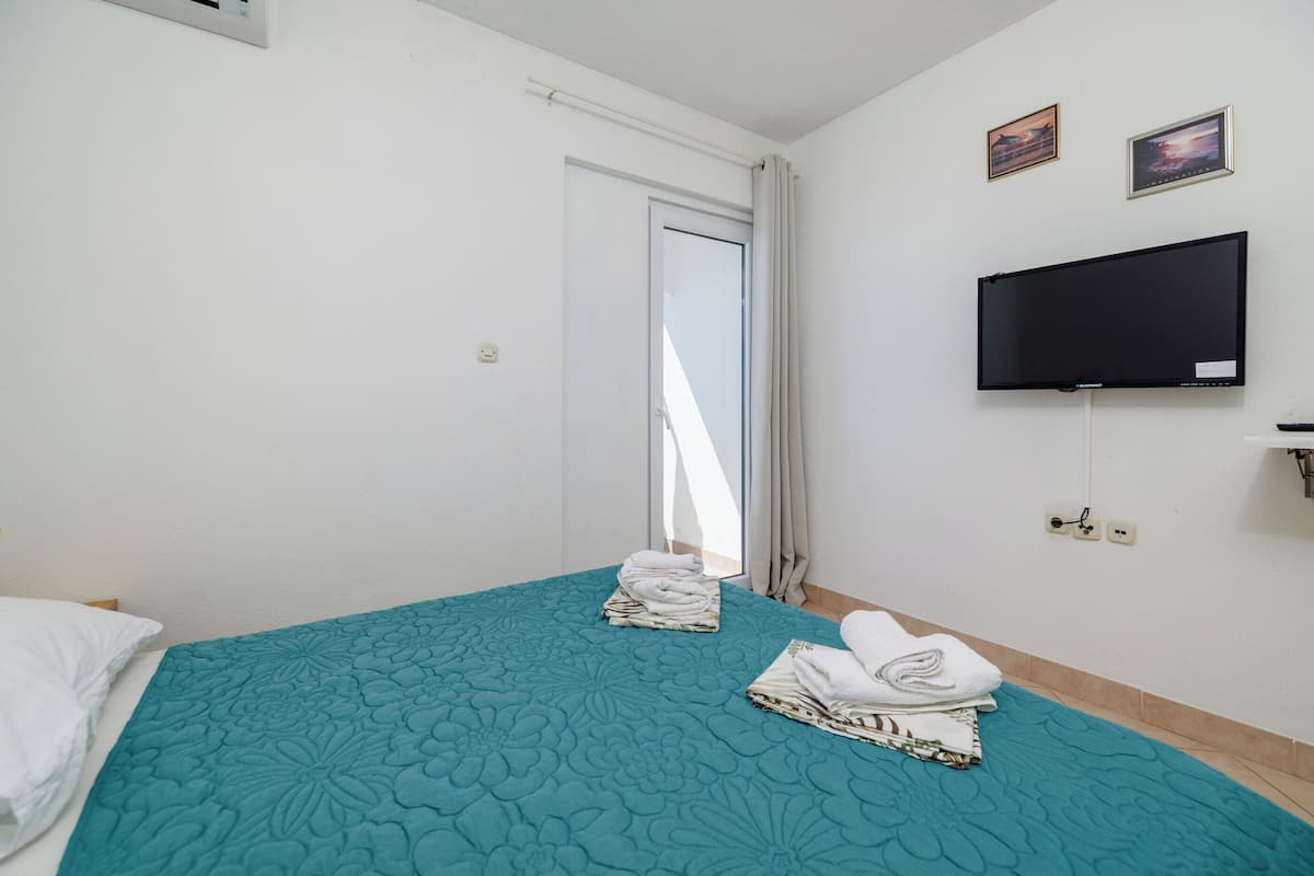 Habitación de hotel con una colcha color turquesa, un televisor de pantalla plana en la pared y una puerta que da a un balcón.