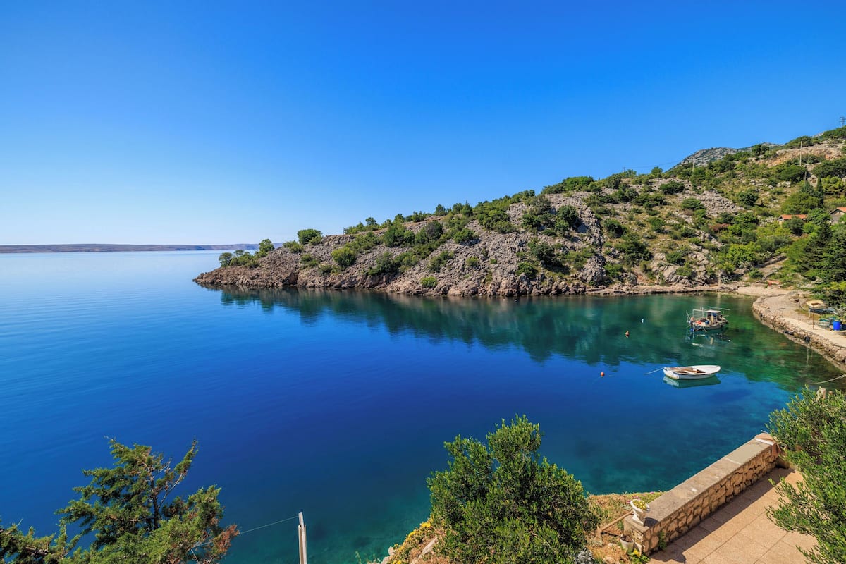 Un paisaje costero con aguas azules cristalinas, terreno rocoso y un pequeño barco amarrado cerca de la orilla.