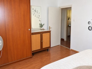 Une chambre à coucher avec une armoire en bois, une table de chevet ornée d’un vase et d’une bougie, et un lit recouvert d’une couverture à motifs.
