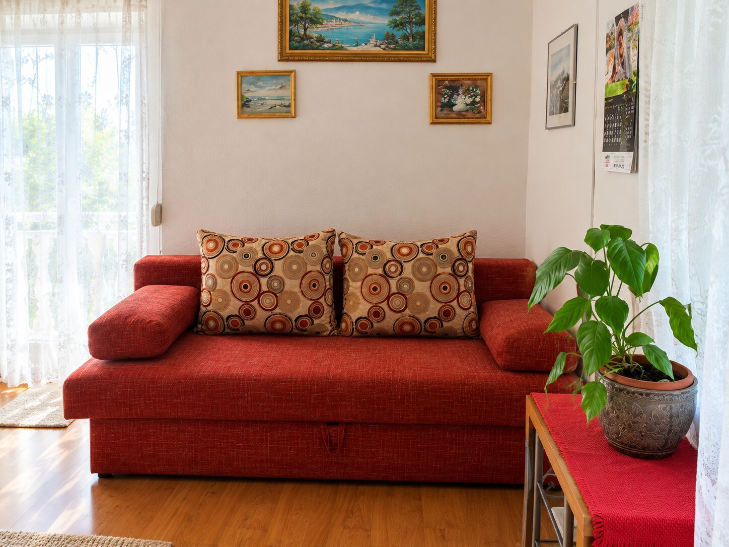 Un sofá rojo con cojines estampados, una planta en maceta y obras de arte en las paredes.