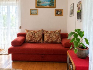A red sofa with patterned cushions, a potted plant, and artwork on the walls. - Apartment Ralje (Sali)