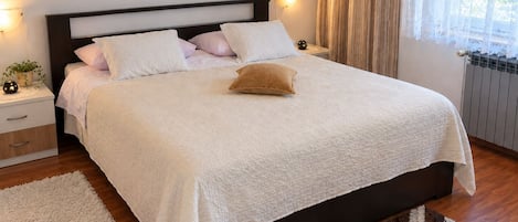 Un lit bien fait, recouvert d’une couette blanche, avec un oreiller marron et une table de chevet sur laquelle se trouvent une lampe et une petite plante.
