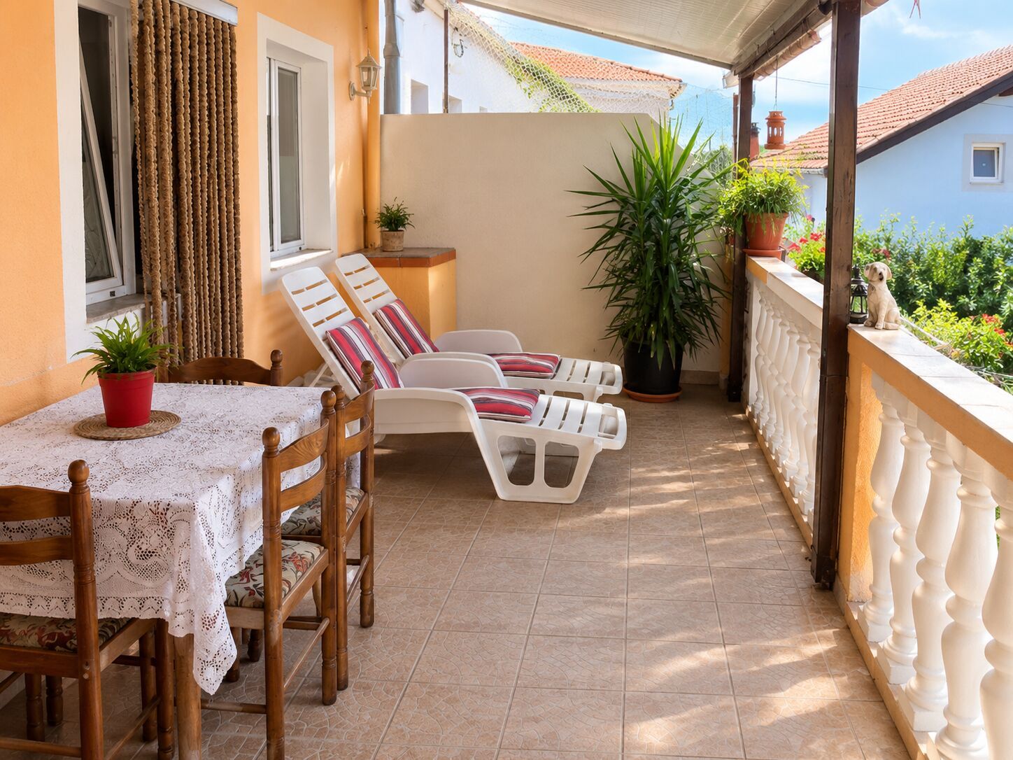 Un balcone con due poltrone, un tavolo con tovaglia di merletto e piante in vaso.
