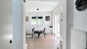 A modern kitchen with white cabinets, a dining table with chairs, and a view of the outdoors through the window. - Apartment Matija (Tisno)