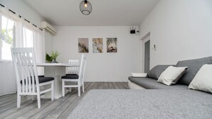 A modern, minimalist room with a grey sofa, two white chairs, a small table, and three wall art pieces. - Apartments Gabi i Miki (Trogir)