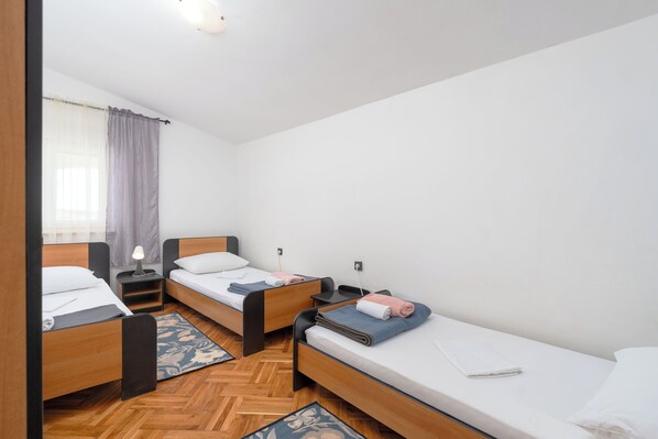 A room with three wooden beds, each with a nightstand and a lamp. - Apartments Bozica (Vir)
