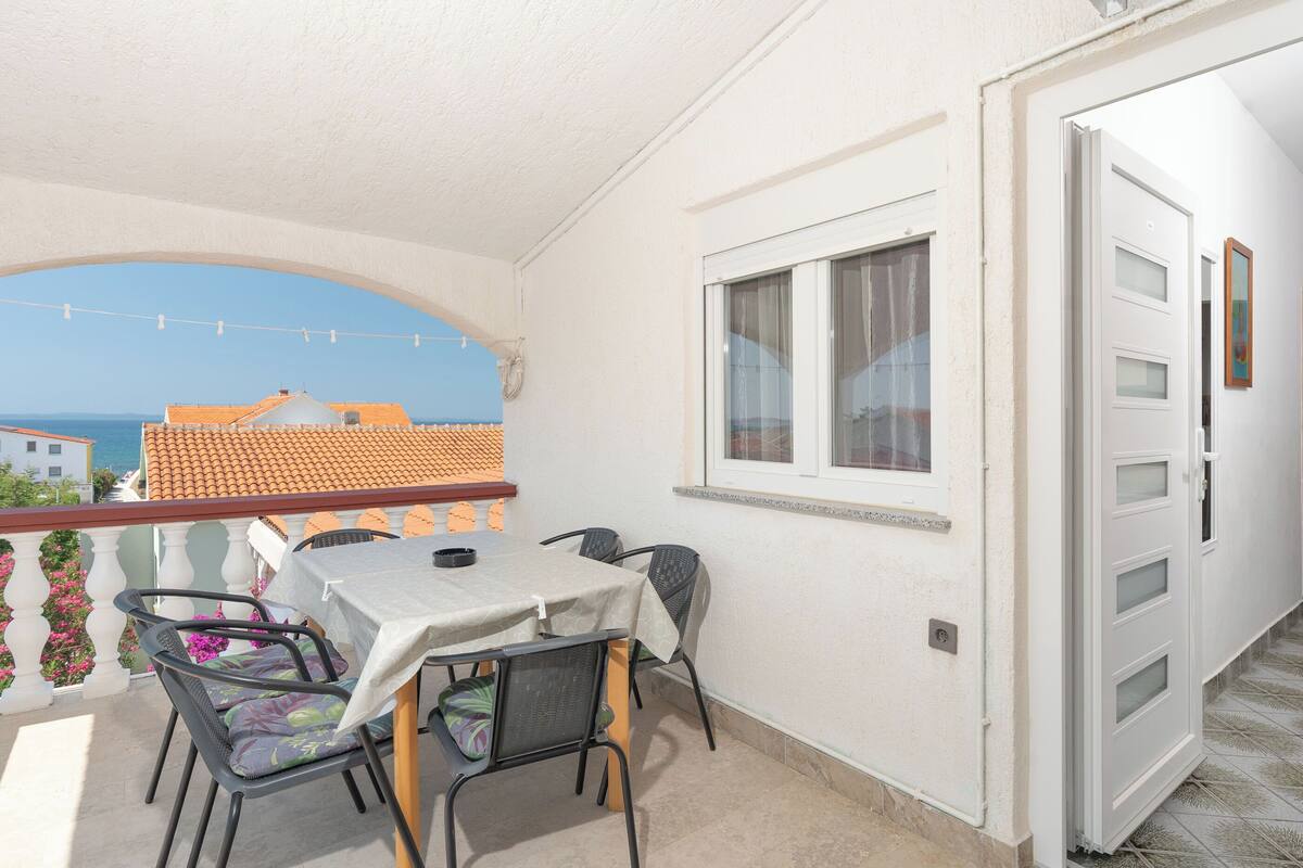 A balcony with a table and chairs, a view of the sea, and a door with a window.