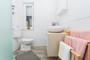 A compact bathroom with a toilet, sink, and a small window. - Apartment Knez 1 (Podstrana)