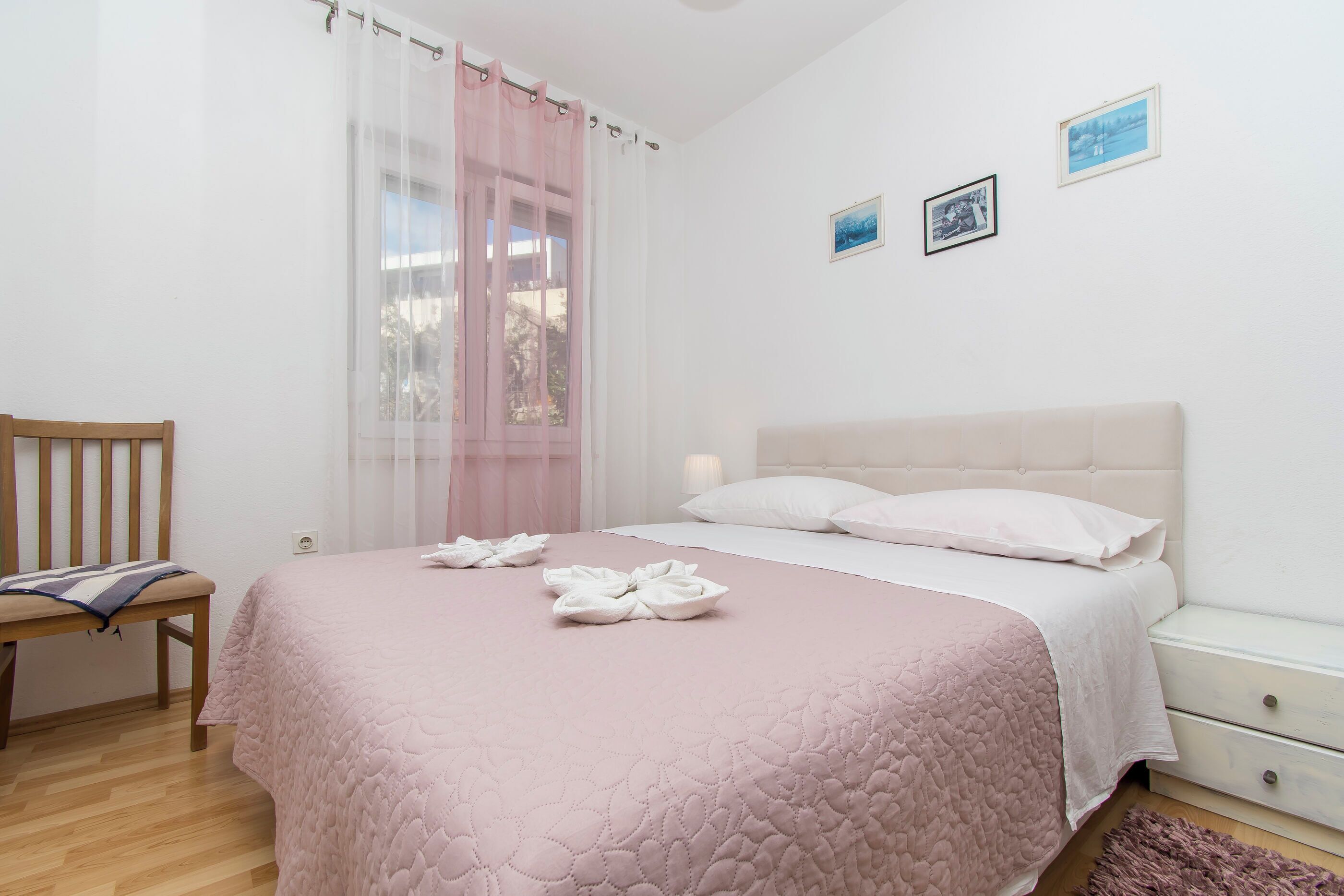 A bedroom with a bed, a chair, a nightstand, and a window with curtains.