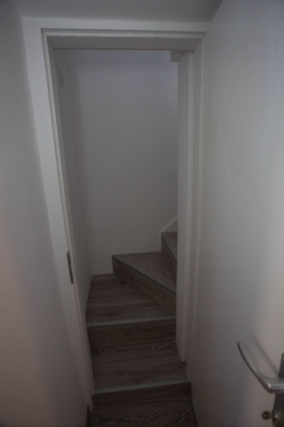 A narrow hallway with wooden stairs leading to a door.