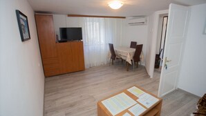 Un soggiorno con televisore su un mobile in legno, un tavolo da pranzo con sedie e una bacheca con documenti.