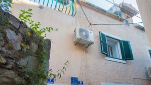 Un vicolo stretto con un muro in pietra da un lato e un edificio con balcone e condizionatore.