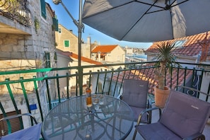 A balcony with a round metal table, two chairs, a potted plant, and a large umbrella. - Apartment Bozo (Split)