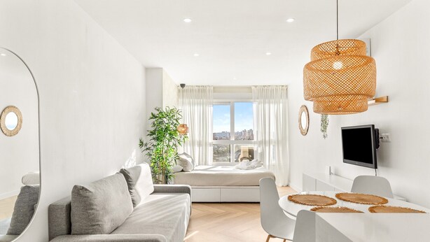A modern living room with a sofa, dining area, and a large window with a city view. - Apartment 'Top Costa Del Sol' with Shared Pool, Wi-Fi and Air Conditioning (Torremolinos)