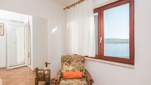 A room with a wooden chair, a small table, a window with a view of the sea, and a door leading to another room. - Apartments Jadra (Novalja)