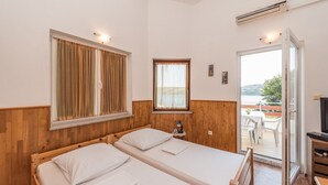 A room with two beds, a small table with a lamp, and a view of the outdoors. - Apartments Jadra (Novalja)