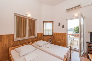 Ein Zimmer mit zwei Betten, einem kleinen Tisch mit Lampe und Blick ins Freie.
