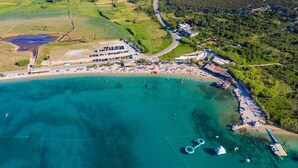 An aerial view of a coastal area with a beach, a parking lot, and a small marina. - Apartments Jadra (Novalja)