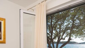 A bedroom with a bed, a window with a view of a tree and water, and a curtain. - House Lucmar (Rogoznica)